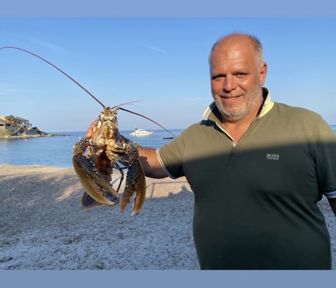 Le père Agostini tenant une langouste sur la plage de Meria